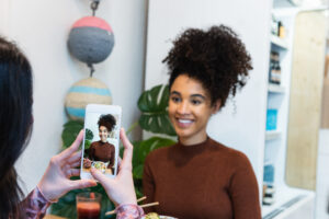 Crop unrecognizable female taking photo of African American friend sitting at table with poke dish in restaurant