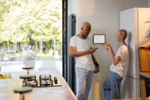  couple controlling smart home devices with a digital tablet on the wall. Concept of modern technologies in domestic lifestyle. Interior of kitchen.